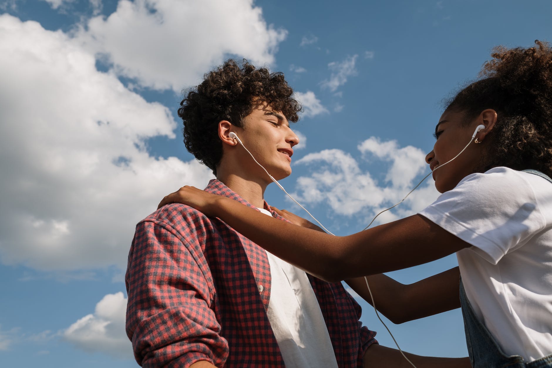 teenage couple sharing headphones against blue sky
